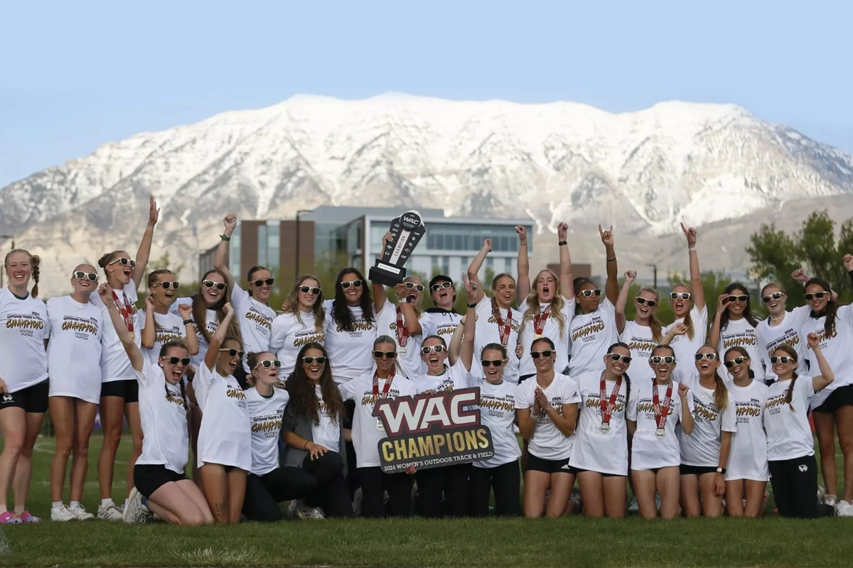 Members of the UVU women’s track and field team pose together on UVU’s Orem Campus, wearing white jerseys and holding their WAC trophy. 