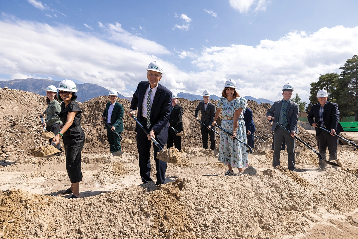President Tuminez, Scott M. Smith, Karen Smith, and other UVU representatives, wear white UVU construction hard hats and shovel dirt during the groundbreaking for the new Scott M. Smith Building. 