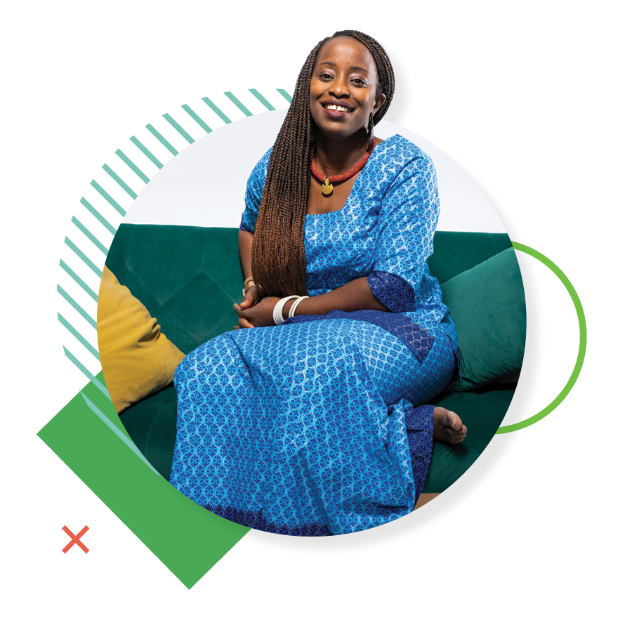 UVU student Yvonne Nsabimana, wearing a blue patterned dress, smiles while posing on a green couch. 