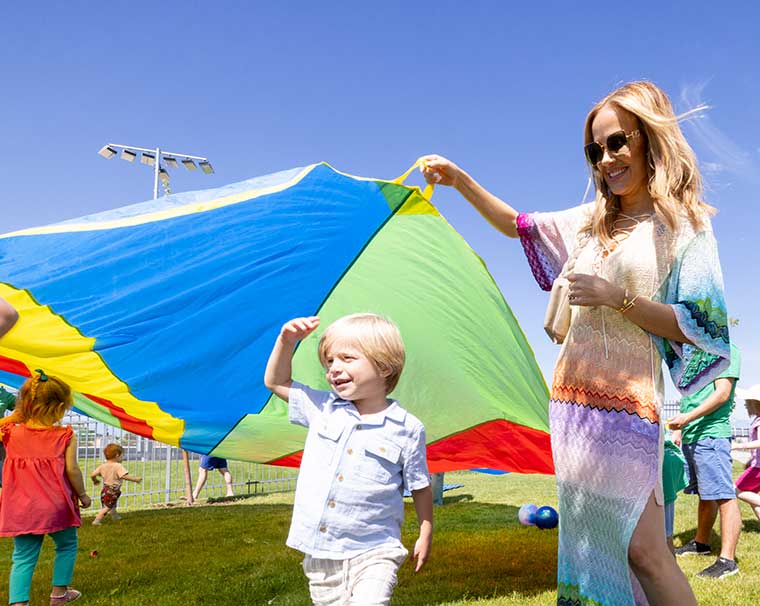 A little girl and guardian enjoy a giant colorful parachute at Uplifting Celebration for Autism.
