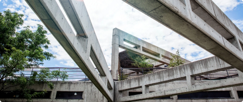 Concrete architectural structure with intersecting beams and a view of the sky and trees.