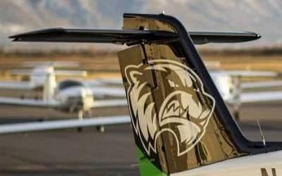 Tail of a small aircraft with the UVU athletic logo. Plane is on the ground