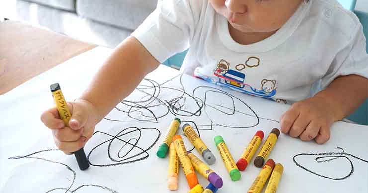 El niño está coloreando en una hoja grande de papel con crayones de colores.