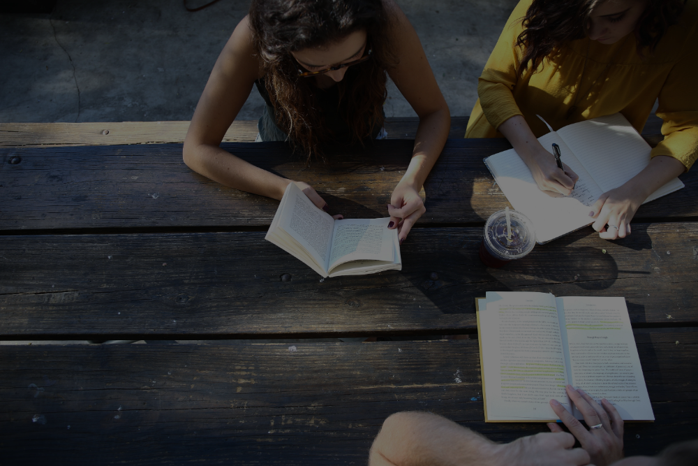 Photo of students reading on a table outdoors