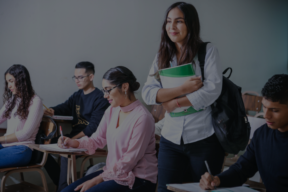 Photo of a student walking towards the front of the classroom, with other students in their seats.