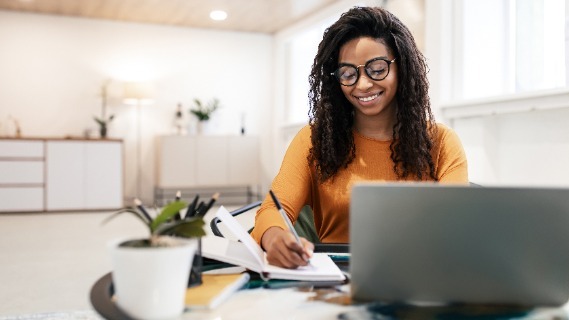 A women working on a computer while taking notes in a notebook