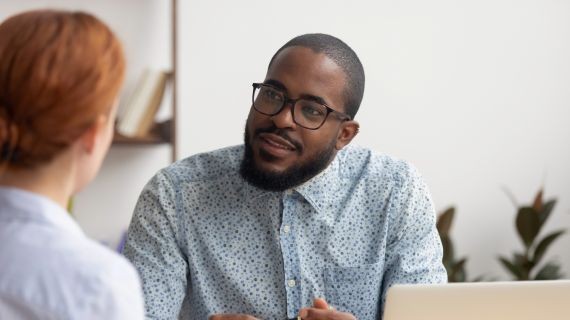 A gentleman sitting at a desk talking to a women sitting on the other side of the desk