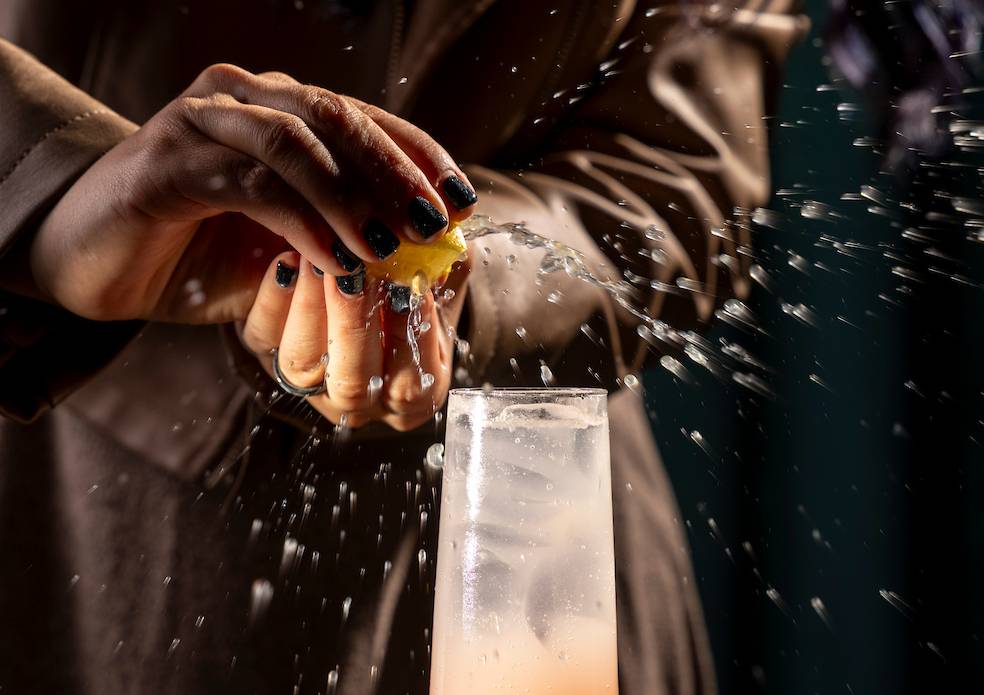 A hand squeezes Lemon into a glass with ice, and a redish liquid