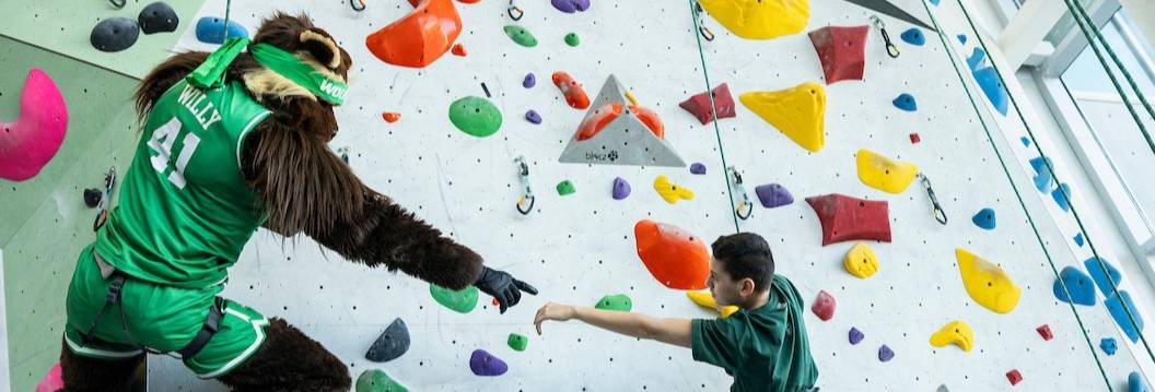 Course Catalog Willy the Wolverine helping a youth climb up a rock wall
