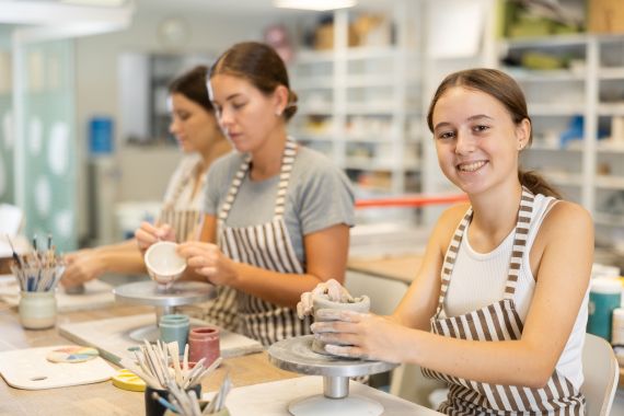 3 individuals wearing stripped aprons while working with clay on small turn tables