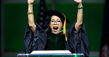 woman in masters graduation robes standing at a podium