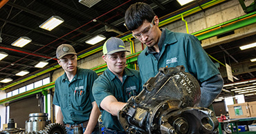 three students working on a large car part