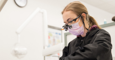 A woman with a mask over her face and dental scrubs on