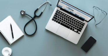 A laptop sits on top of a table with a stethescope next to it