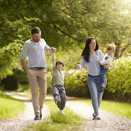 man and woman holding a child on her hip-holding a child's hand as they walk down a forest path