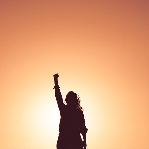 Woman raising a fist in front of a sunset