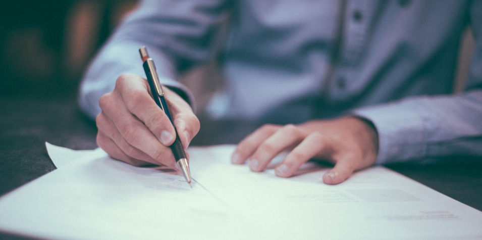 man writing on papers with pen