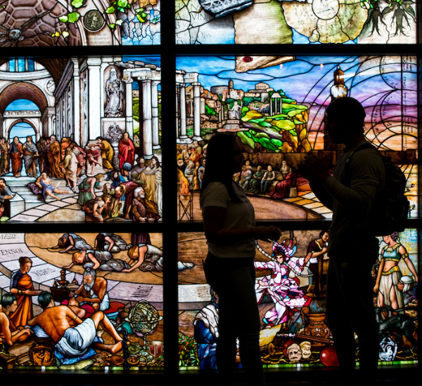 Two students talking in front of the roots of knowledge mural