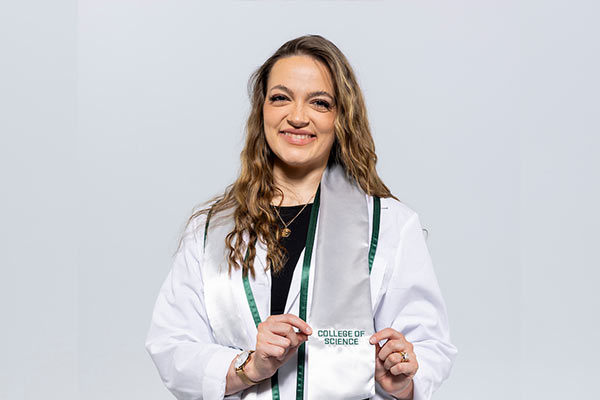 Female wearing graduation clothing, showing stole with "College of Science" written on it. 