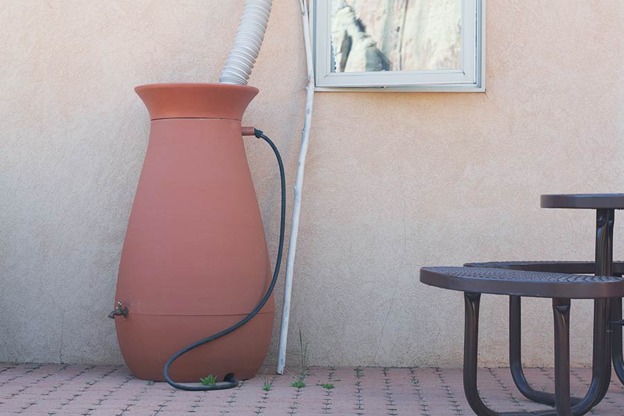 A barrel with a down spout from the roof going inside to store rain water.