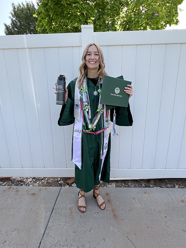 Layton holding her diploma while in her cap and gown smiling.