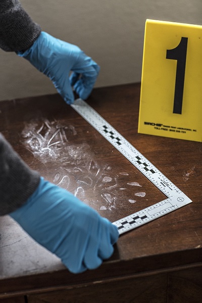 A man measures a dusty footprint on the top of a nightstand