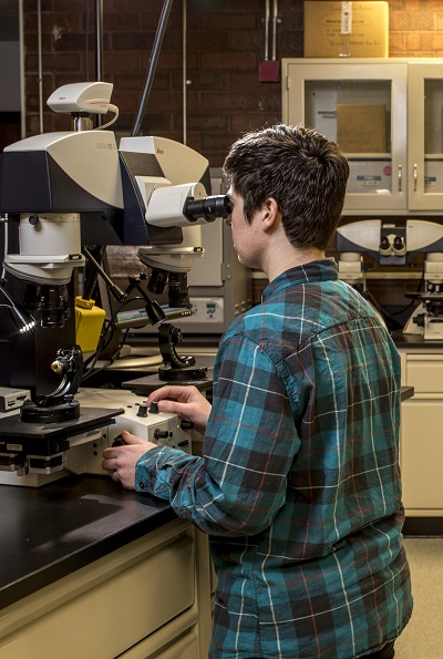 A mean leans into a microscope in the lab