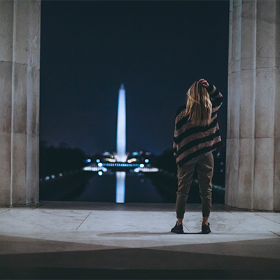woman with her back to the camera looking at the lighted Washington Monument in Washington DC at night