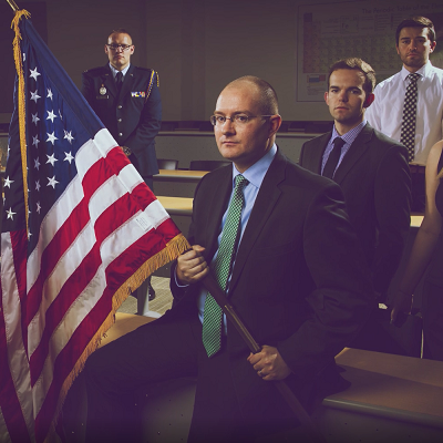 4 men in suits and uniforms at attentions with American Flag