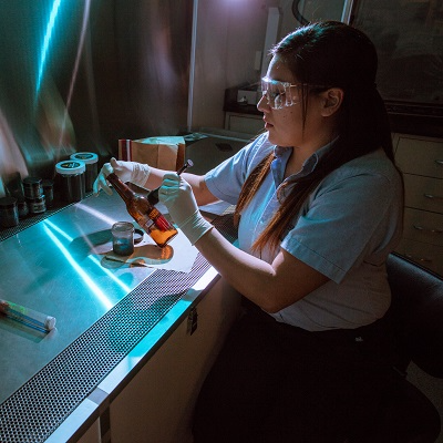 Woman dusting for fingerprints on an empty bottle.