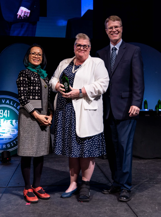 Wendy Farnsworth holding a green award poses between President Tuminez and man