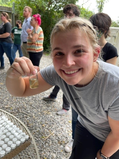 female student holding a small vial with yellow liquid inside the vial.