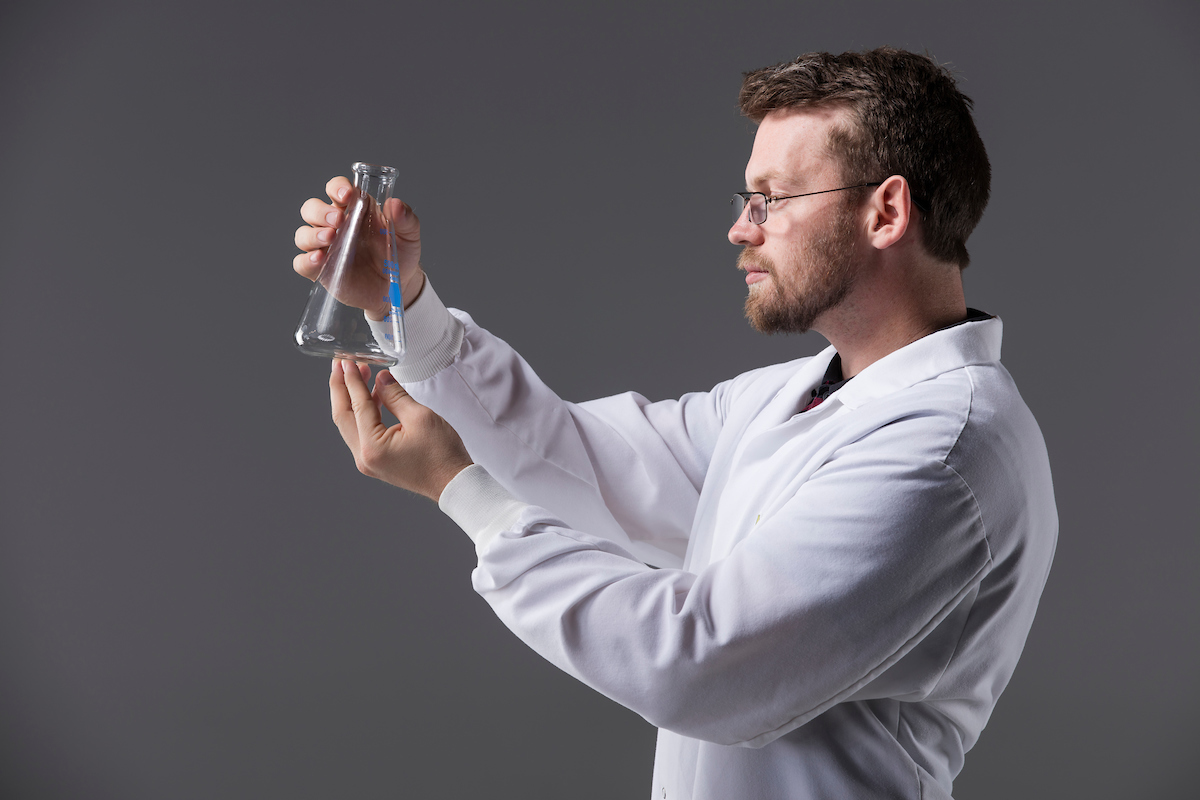 Image of a person in a lab coat looking at a beaker