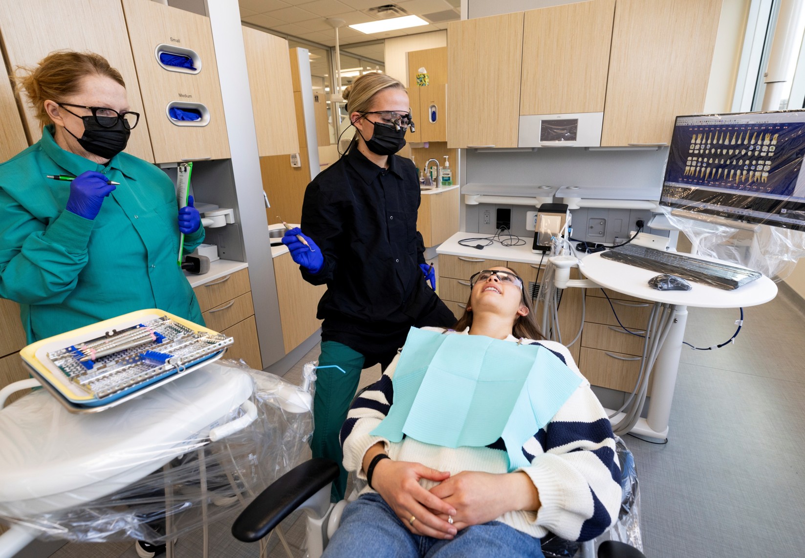 patient in dental chair at UVU Dental Hygiene Clinic patient in chair receiving dental care from dental hygiene student with faculty observing