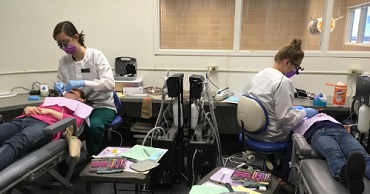 Two students clean two children's teeth