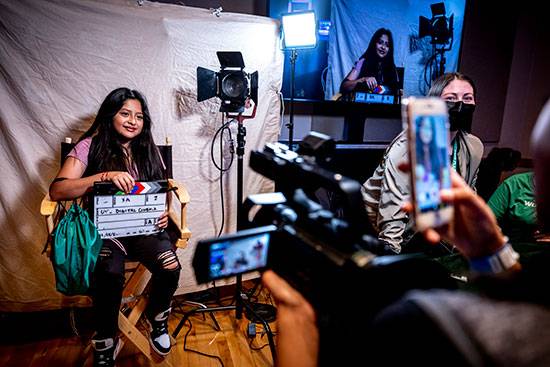 Cinema student Alysha Aldred looks on from the right as a girl sits in the director's chair while her friends take pictures