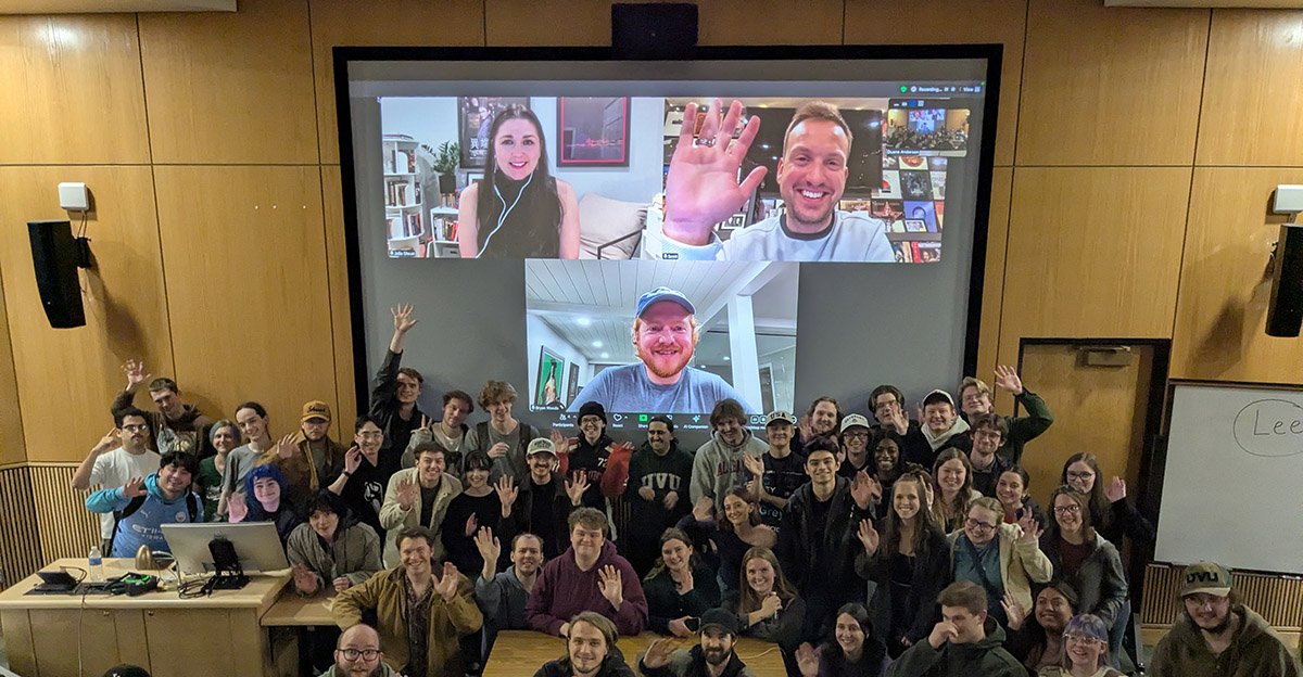 student in a classroom with 3 people on screen using zoom