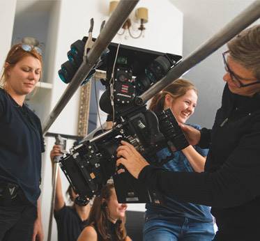 female professional and students adjusting camera on dolly
