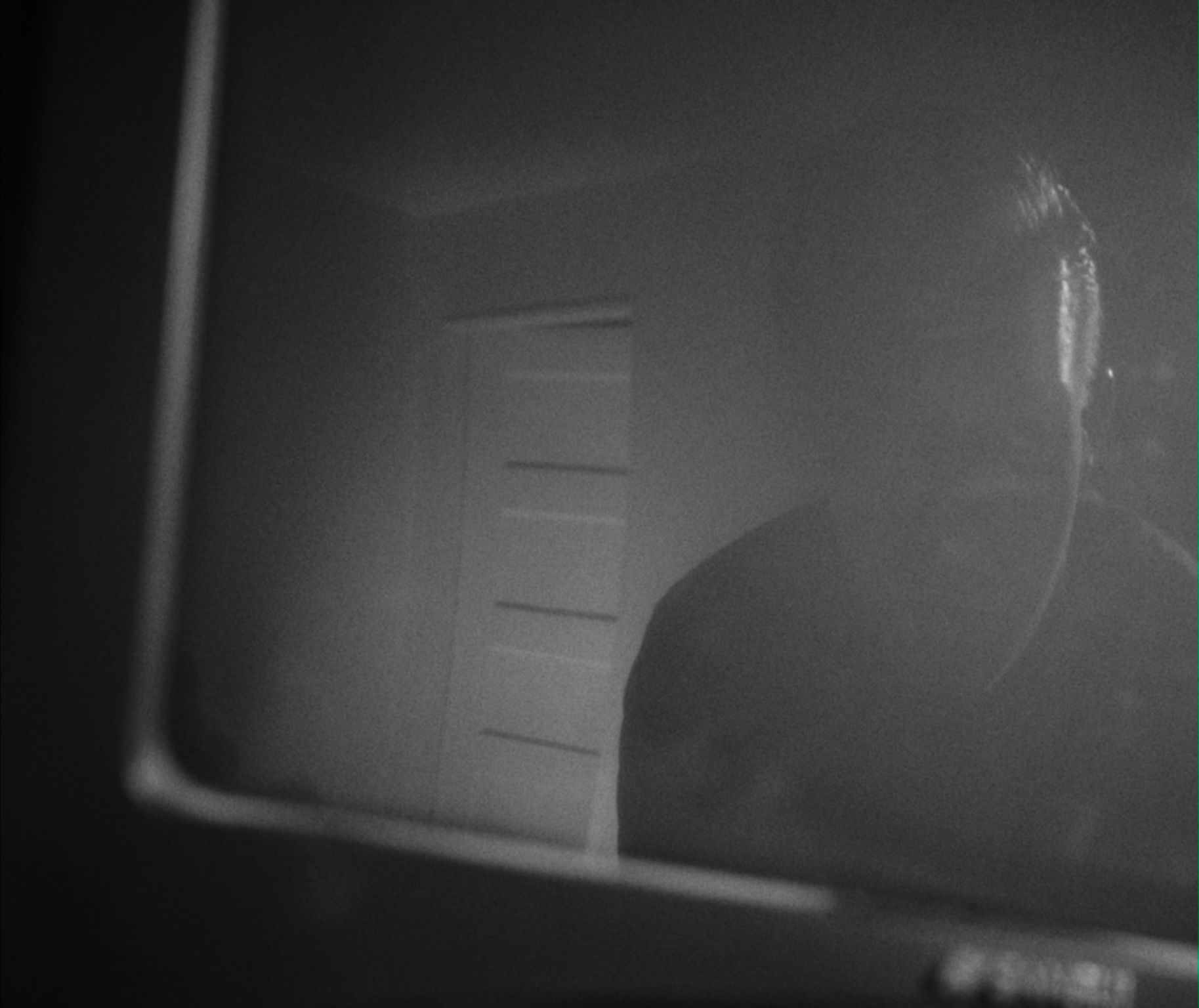 the reflection of a man and a door in the screen of a TV