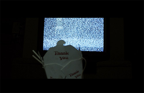 a chinese takeout container backlit by a grainy tv screen
