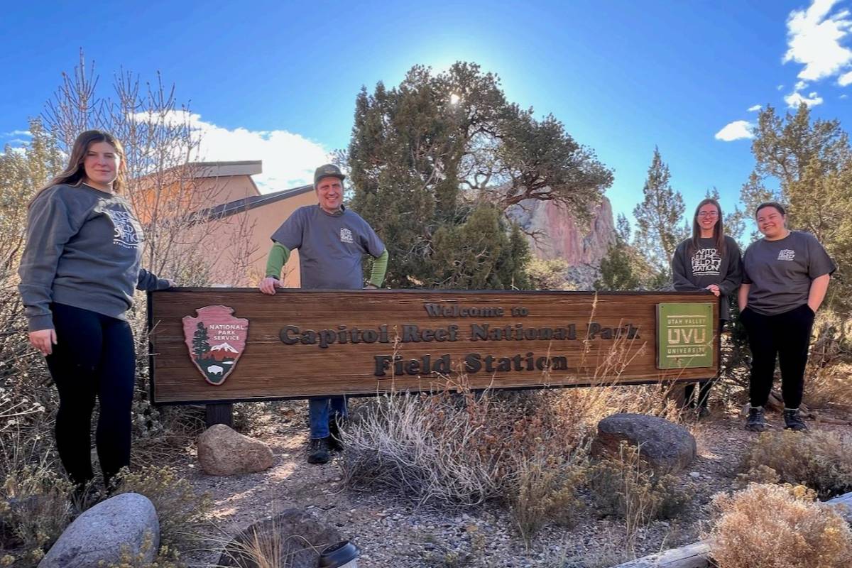 students in front of a wooden sign that says "Capitol Reef National Park Field Station"