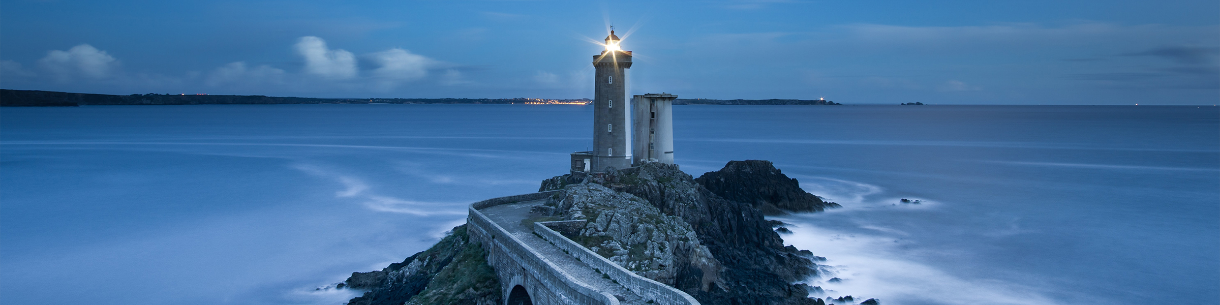 A lighthouse at dusk on a blue beach.