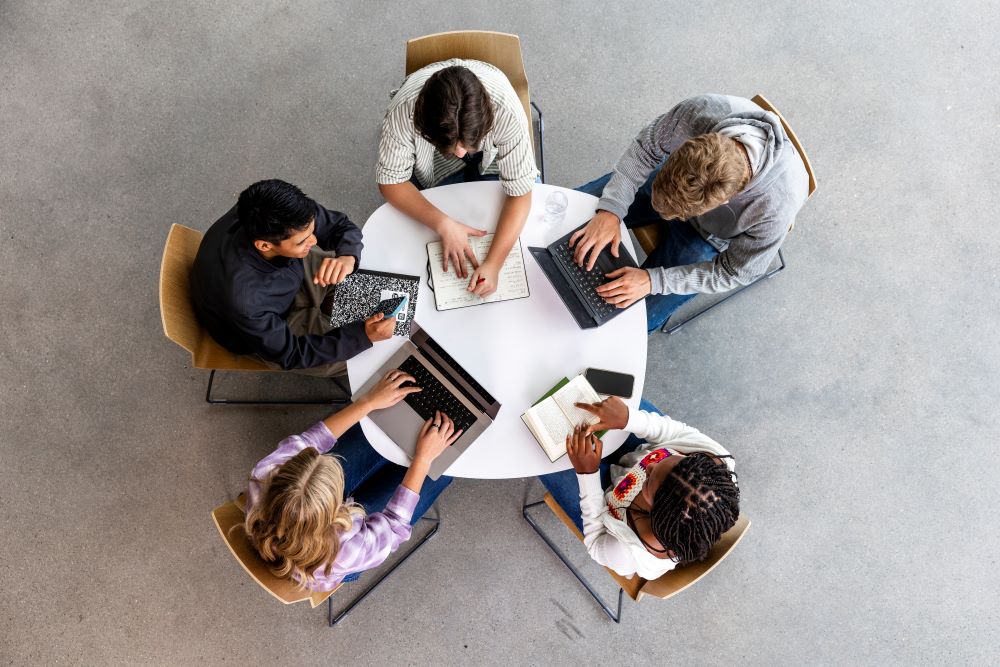 students sat around a table typing on their laptops