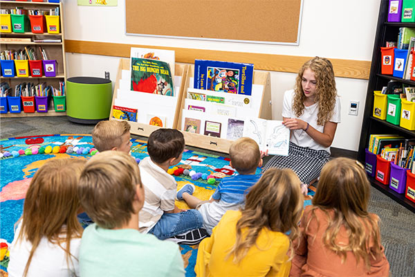 Female teacher reads book to classroom of children
