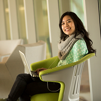 Dark haired female student sitting in a chair with a laptop