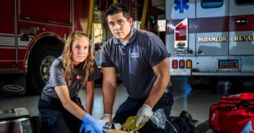 2 paramedics looking at the camera while working on saving a person.