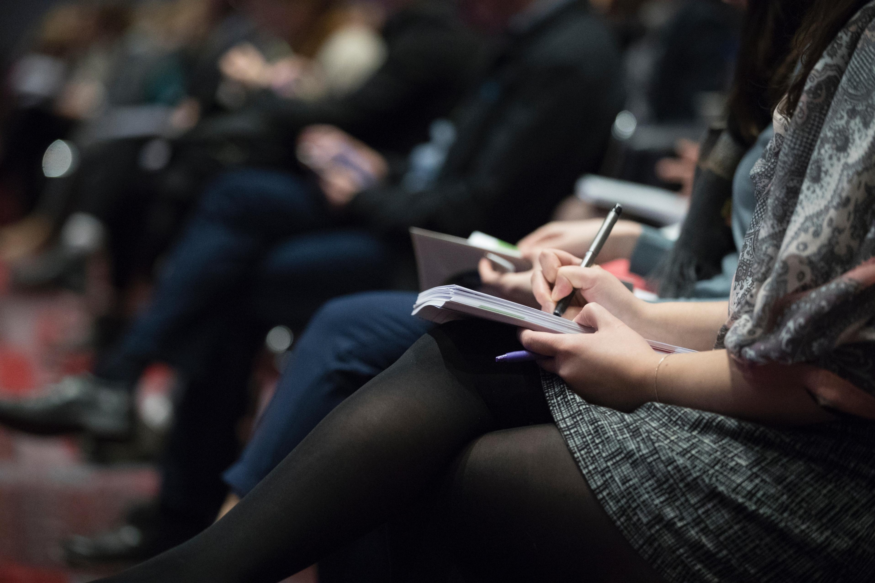 a row of people sitting, with notepads and pens on their laps.