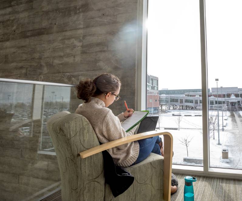 Student sitting in front of a window, with a snowy scene, writing in a notebook.