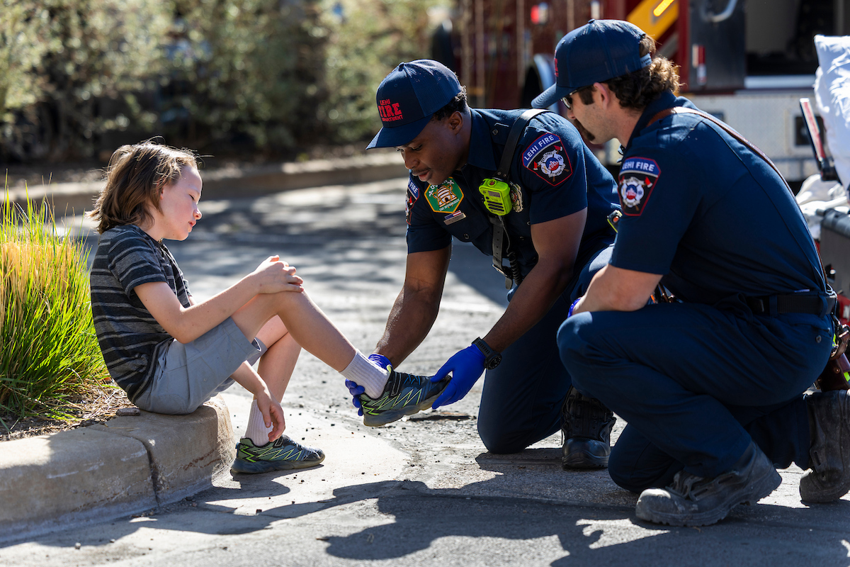 two paramedics kneeling with a child checking out the ankle