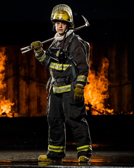 Women Fire Fighter standing epically in front of burning forest. Ax over shoulder.